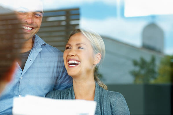 young woman and man laughing holding a piece of paper looking out the window