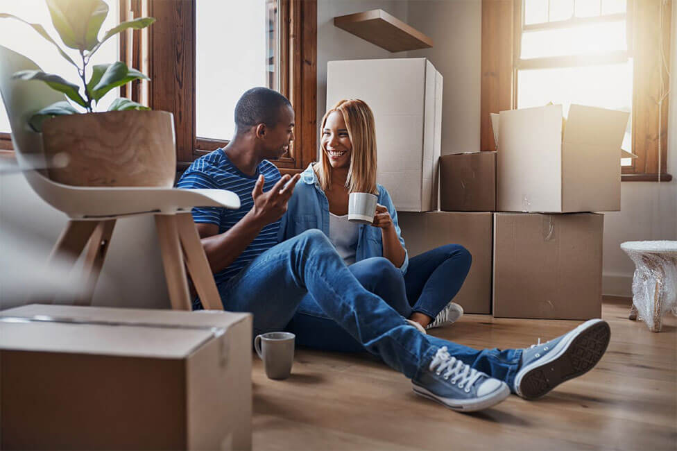 young couple sitting on the floor of their home smiling and talking