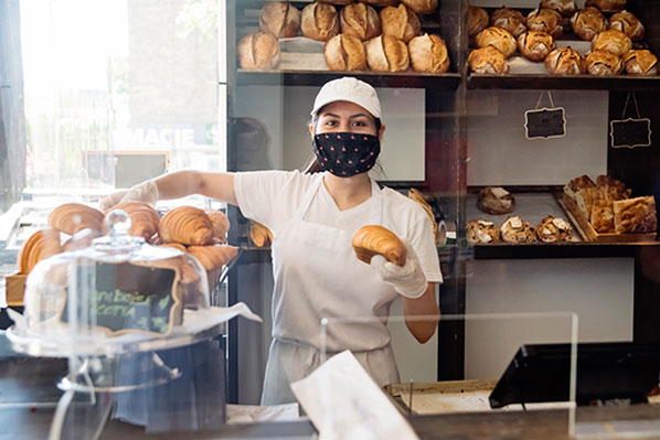 young female bakery owner holding fresh croissants behind the counter