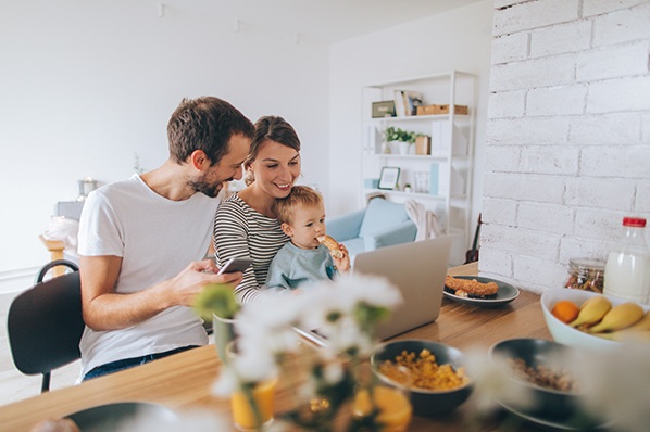 young mom and dad having breakfast at the kitchen counter holding a toddler