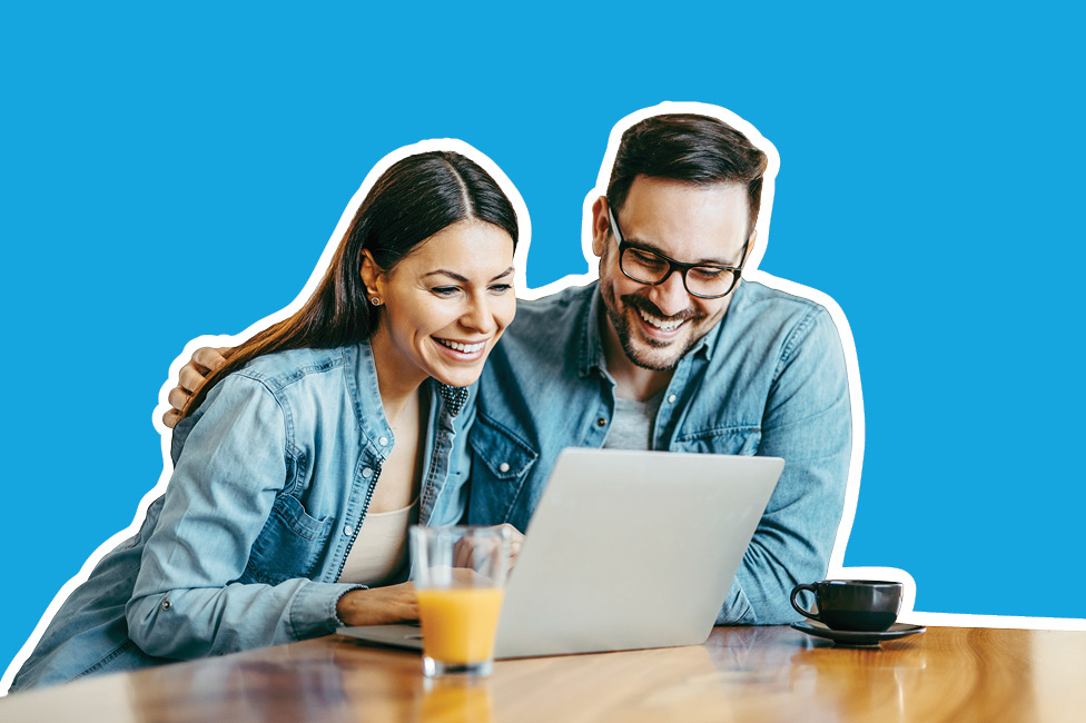 smiling couple sitting at the table looking at their laptop