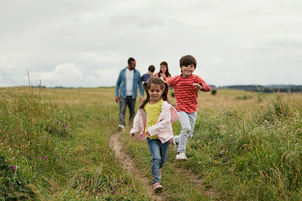 young family out for an outdoor walk in a field with two little kids running ahead of their parents
