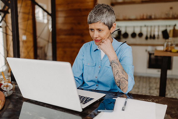 middle-aged person with short hair and wearing a blue button shirt looking at their laptop