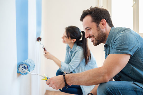 a couple in their 30s painting a wall blue together