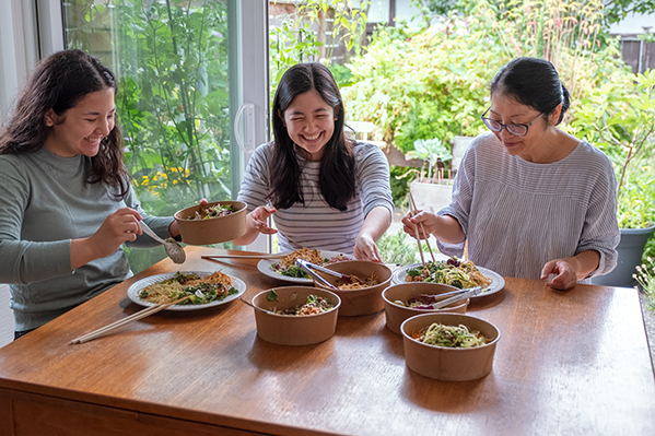Mother and two daughters have ethnic food at kitchen table.