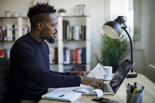 image of an adult black male on his laptop with notebook and printouts in hand