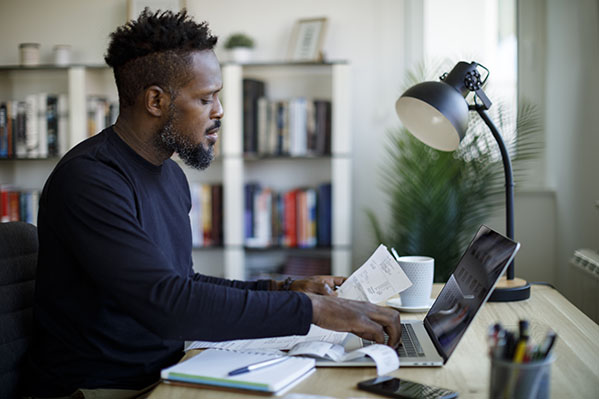 Adult male sitting at desk while reviewing his expenses and inputting them into a laptop.