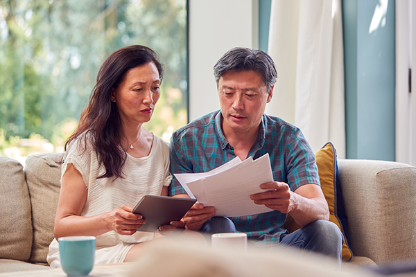 middle aged husband and wife looking at paperwork sitting together on the couch