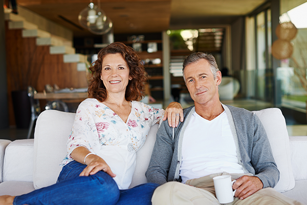 middle-aged Caucasian couple sitting on their living room couch smiling at the camera