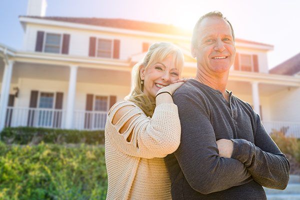 middle-aged older couple outside of their large family home smiling looking at the camera