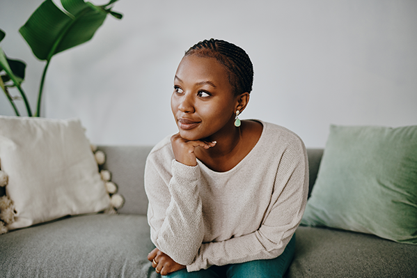 An pensive woman sitting on a couch, hand on chin, smiling