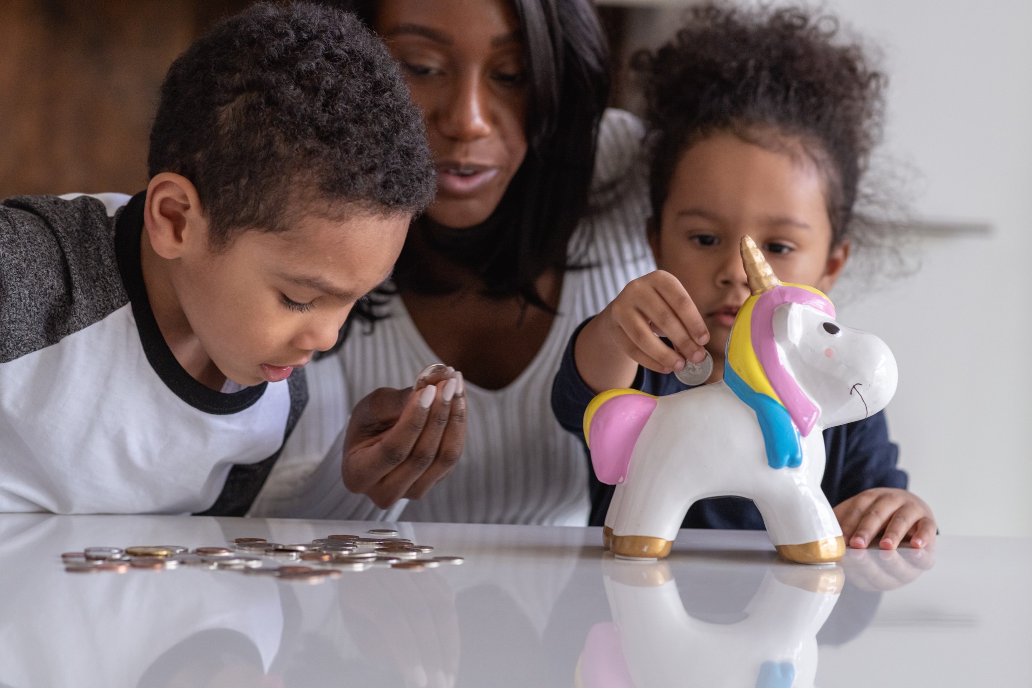 mom with young daughter and son putting coins into a unicorn piggy bank