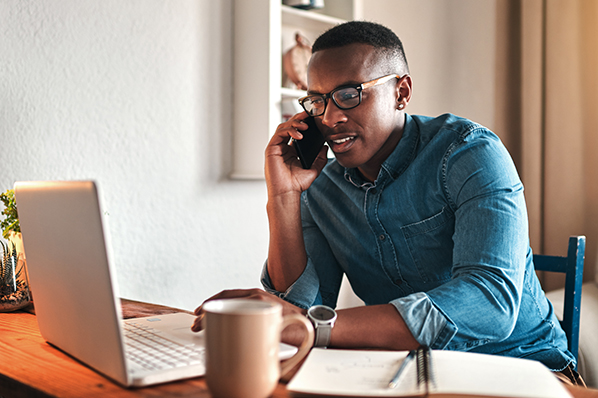 young man chatting on his phone while looking at his laptop