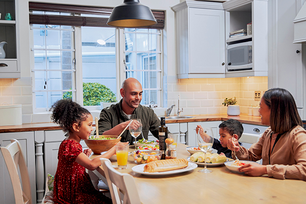 Family of four sitting down at kitchen table to have a healthy, homemade meal.
