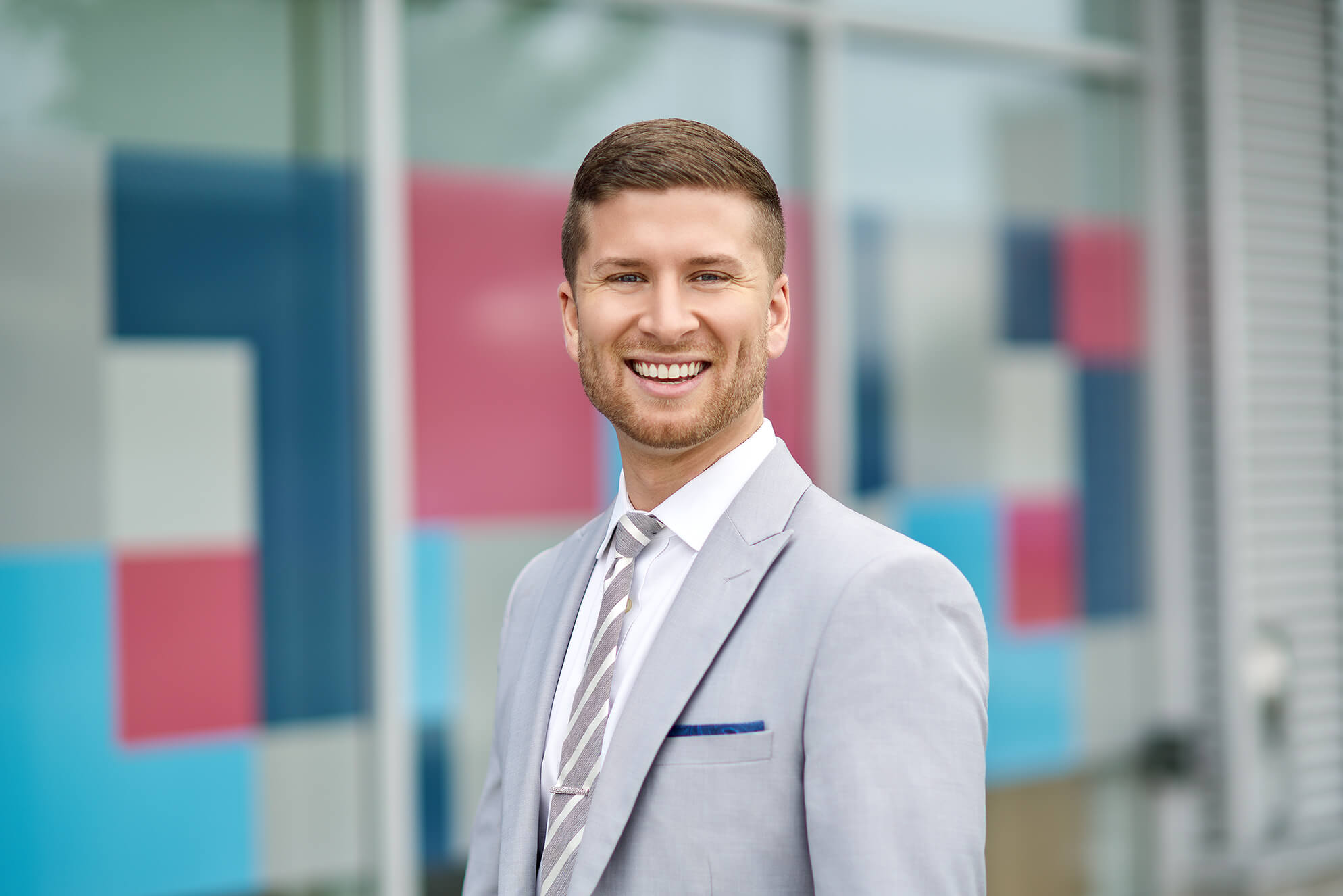 Image of Mitch Romano in a light grey suit smiling at the camera