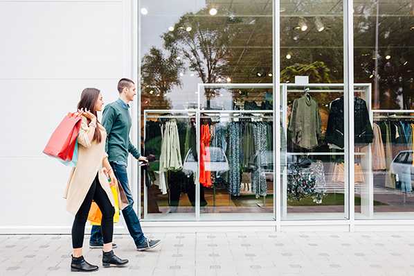 young couple walking in front of a store front window with shopping bags