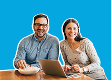 smiling couple sitting at the table looking at their laptop