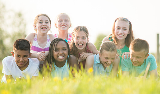 8 kids laying down in grass smiling at the camera