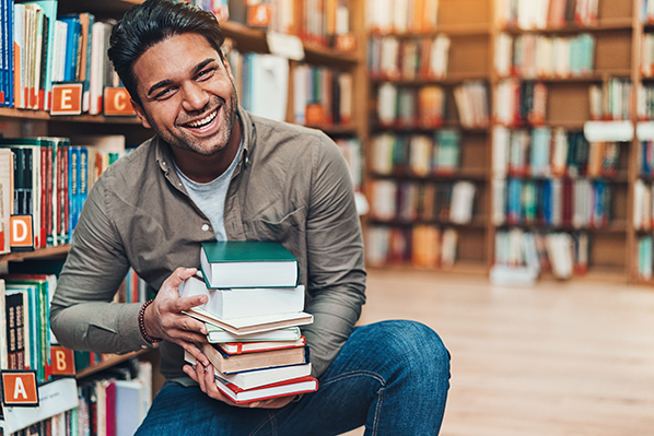 young man smiling and holding a stack of books in the library.jpg
